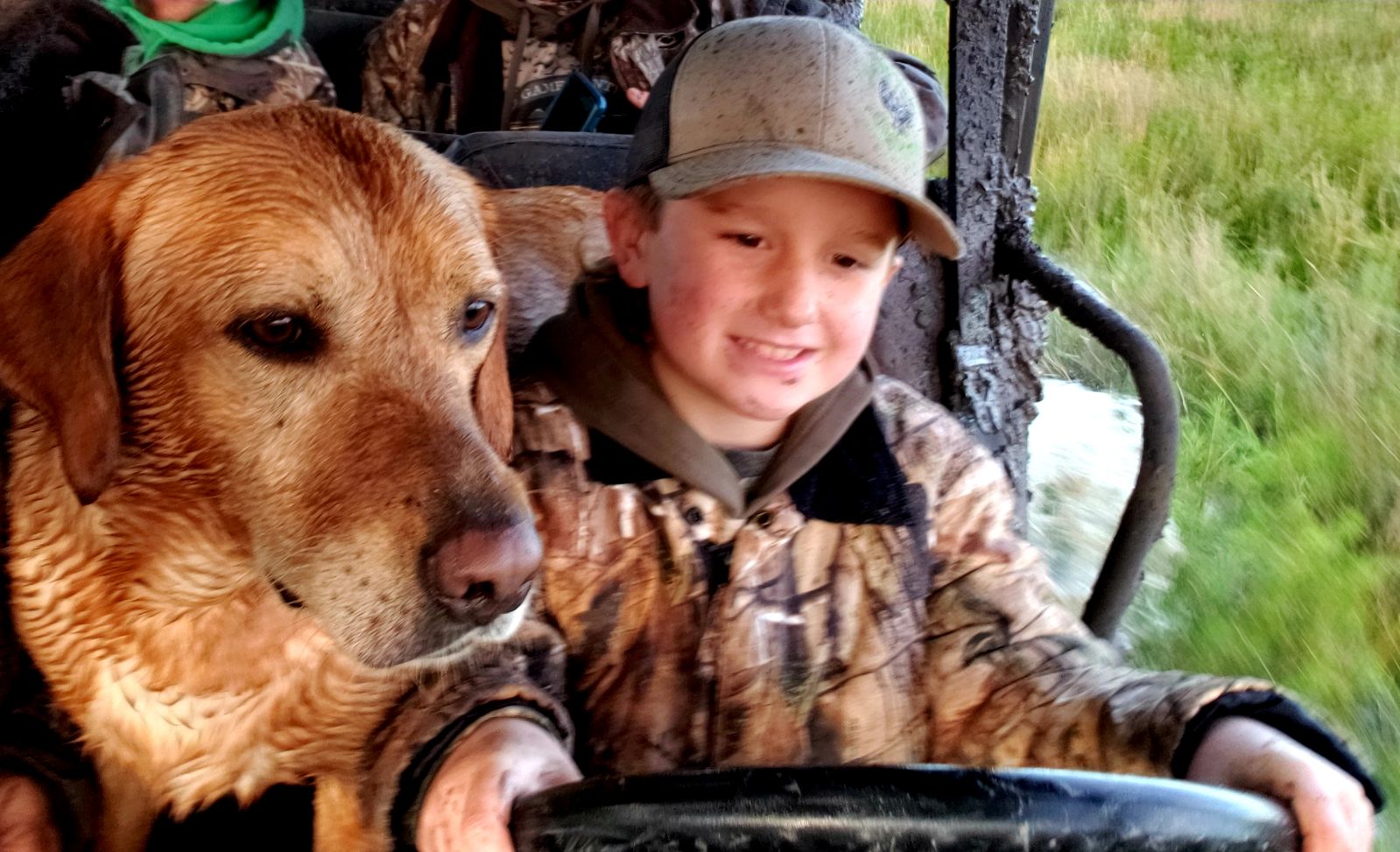 Young hunter riding beside a wet yellow Labrador Retriever in the field